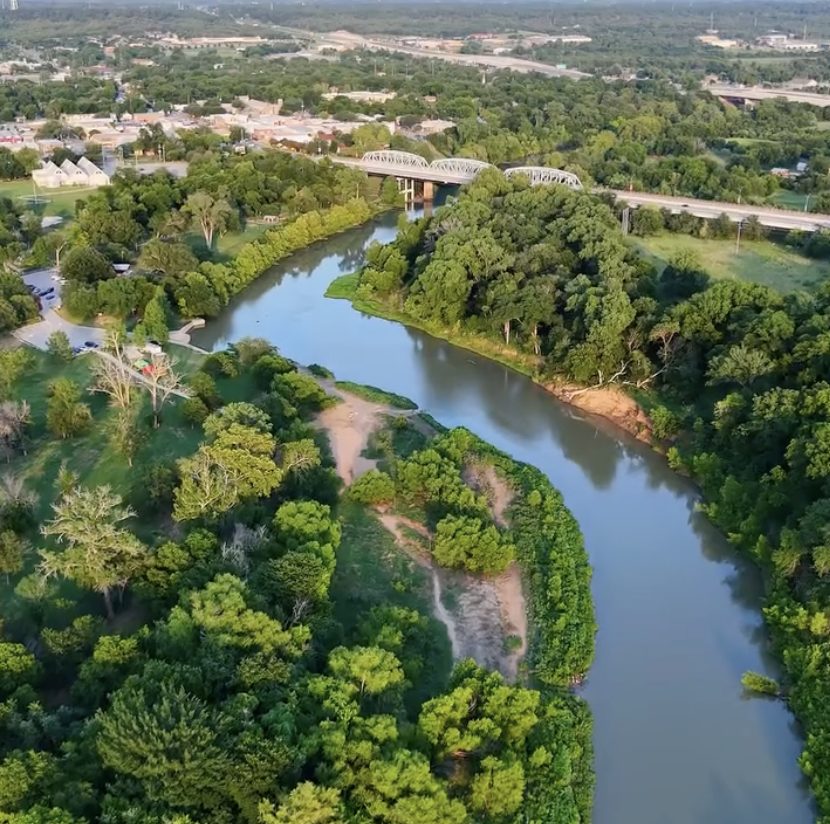Aerial view of the Colorado River winding through green trees past downtown Bastrop